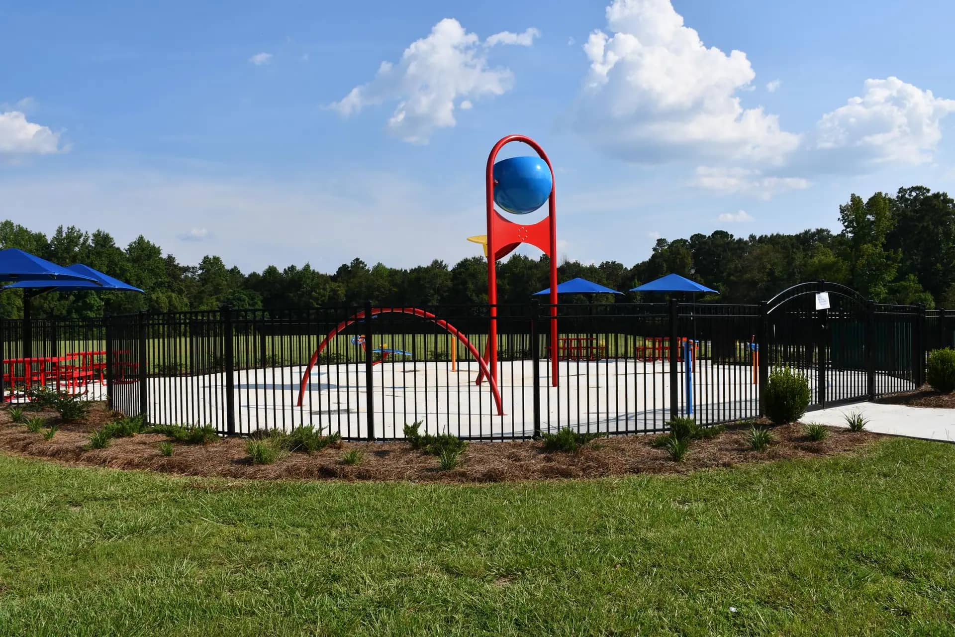 Red and blue water-play structures inside the fenced Richton Splash Pad