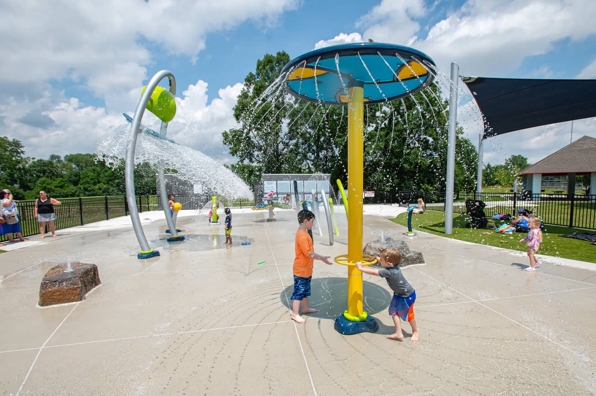 Families using the umbrella cascade, spray arches, and ground jets at Bicentennial Park Splash Pad